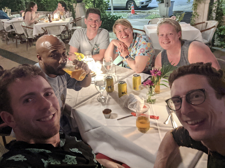 Smiling selfie of a group of people at an outdoor dinner table.